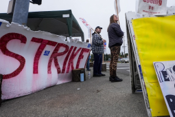 Two workers staff a picket line with a giant red ‘strike’ sign and a “Pension or Bust” sign.