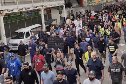 Hundreds march though an industrial plant, one sign reads: Historic Slap in Our Faces