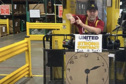 A worker on a forklift points to his watch with a clock sign below him.