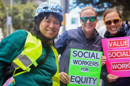 Three women hold signs saying “Social Wokrers for Equity” and “Value Social Work”