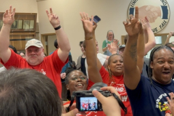 Several people raise their fists indoors, they look excited and happy.