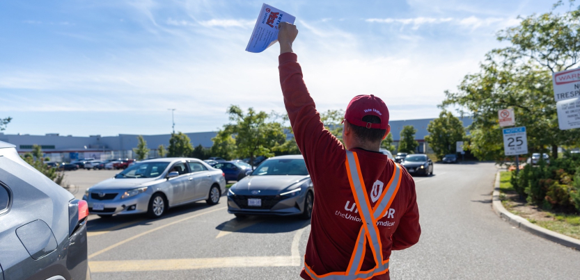 A worker holds a flyer in the air. His hat reads: "Vote Unifor"