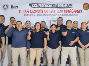 St Gobain workers stand in front of a large banner reading: Press Conference—The Day After Contract Legitimations; Advances and Challenges in Independent Unionism