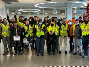 A group of Amazon workers wearing yellow hi-vis vests stands together after marching on their boss.