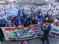 a crowd of educators wearing coats and matching blue MFT knit hats hold picket signs and a banner that reads "districts refuse to pay for ESPs, our children need heroes."