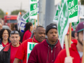 A group of UAW members march holding picket signs that say "UAW On Strike."