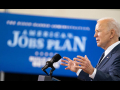 sideview of President Joe Biden speaking at a podium at Pittsburgh Carpenters Hall on March 31, 2021, with American Jobs Plan sign in background (white on blue)