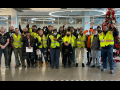 A group of Amazon workers wearing yellow hi-vis vests stands together after marching on their boss.