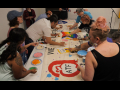 Several people work around a table adding colorful paints to a banner. Photo: ATF