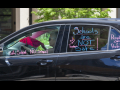 A woman drives a car with the words "Schools are not safe!" "I love teachers" and "People over profit" painted on the windows