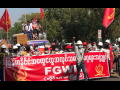 Dozens of workers march behind a red banner in Myanmar. Some carry red flags.