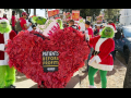 Two people in green Grinch suits hold a giant paper-mache heart that contains a "patients before profits" sign. Behind them an NUHW Kaiser picket line crowd is visible.