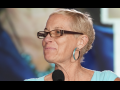 Photo of Jane McAlevey smiling at a microphone and looking left in an aqua blue shirt