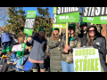 Women stand on a sunny day, wearing big jackets, holding green printed ONA picket signs that say "Unfair Labor Practice Strike" and "Nurses on Strike." A handmade sign visible in the background says "Burnout caused this turnout."