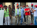 A group of mainly Pakistani immigrant workers stand at a rally while a union organizer speaks through a bullhorn.