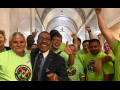 Happy people in neon yellow RDU shirts, plus a man in a suit, raise jubilant fists in a legislative hallway