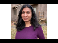 Sindhu poses outside in front of a barn. She has long black hair and is wearing a red shirt and a slight smile.