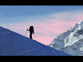 Silhouette of a skier ascending a mountain slope with pink sky in background