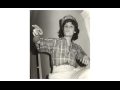 Black-and-white photo looks upward at a woman in a plaid shirt and bedazzled hardhat, gesturing and speaking