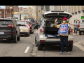 woman in front of the back of her car, trunk open, standing with a save usps sign.