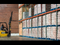 Worker with forklift in front of cases of pallets on shelves in warehouse