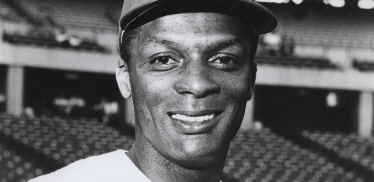 Center fielder Curt Flood smiles in a close-up head shot with stadium seating behind him.