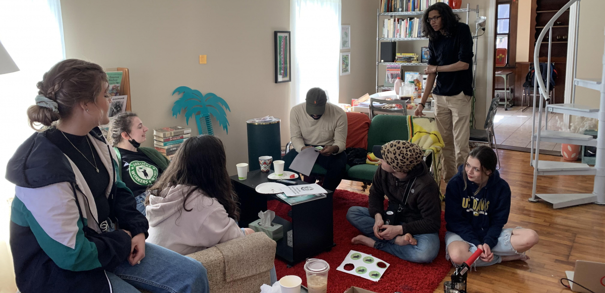 A group of Chipotle workers and supporters gather around a coffee table at a house to discuss their campaign.