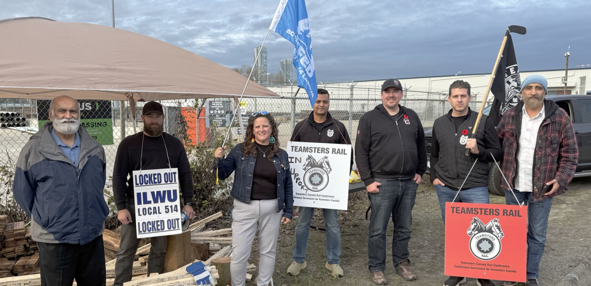 A group of people hold picket signs in front of a canopy.