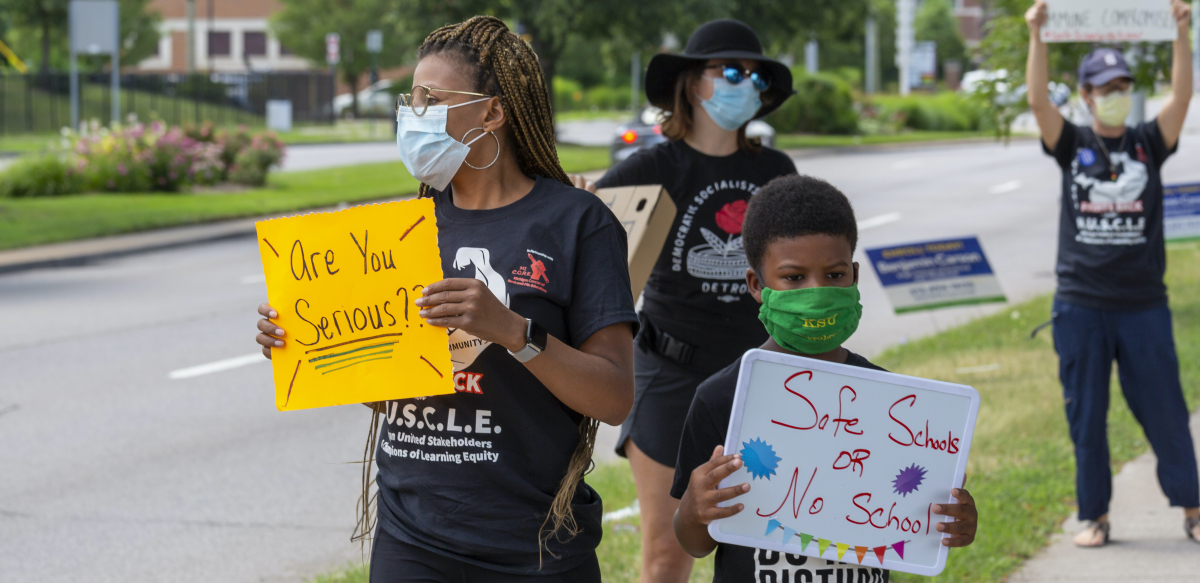 A woman holds a sign that says "Are you serious?", while her son holds a sign reading "Safe schools or no school."