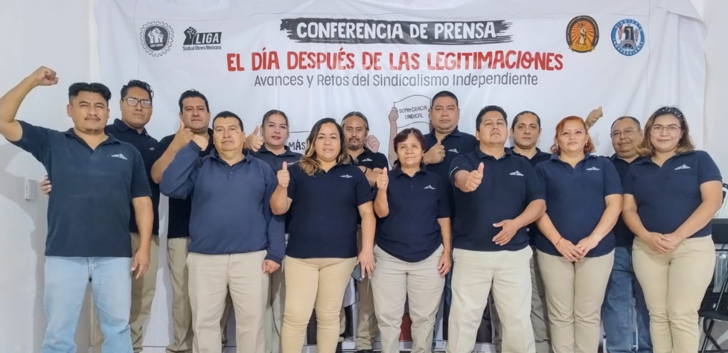 St Gobain workers stand in front of a large banner reading: Press Conference—The Day After Contract Legitimations; Advances and Challenges in Independent Unionism