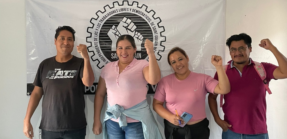 Four members of the bargaining committee at Saint Gobain pose in front of their union's banner.