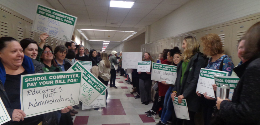 Brookline paraeducators with signs lining hallway of school.