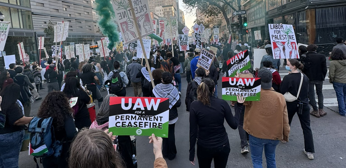 Marchers march away from the camera with signs reading UAW for a Permanent Ceasefire