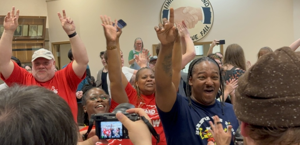 Several people raise their fists indoors, they look excited and happy.