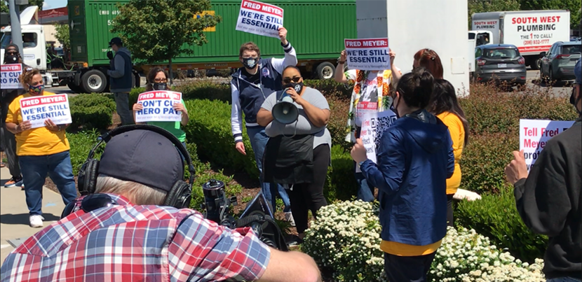 Woman with bullhorn surrounded at safe social distance by supporters with signs. Cameraman in foreground bottom left taking video.