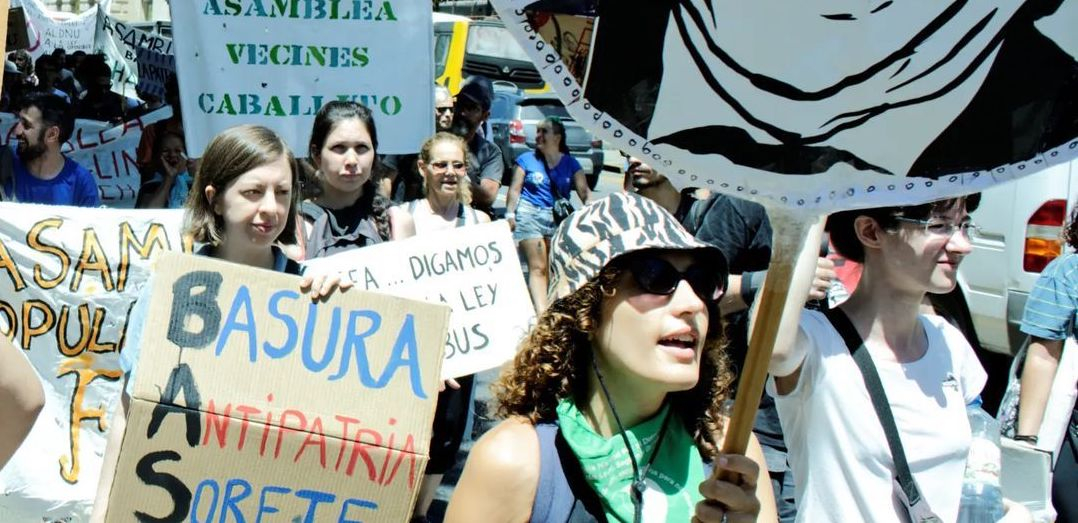 Several people with banners in Spanish march towards the camera’s right