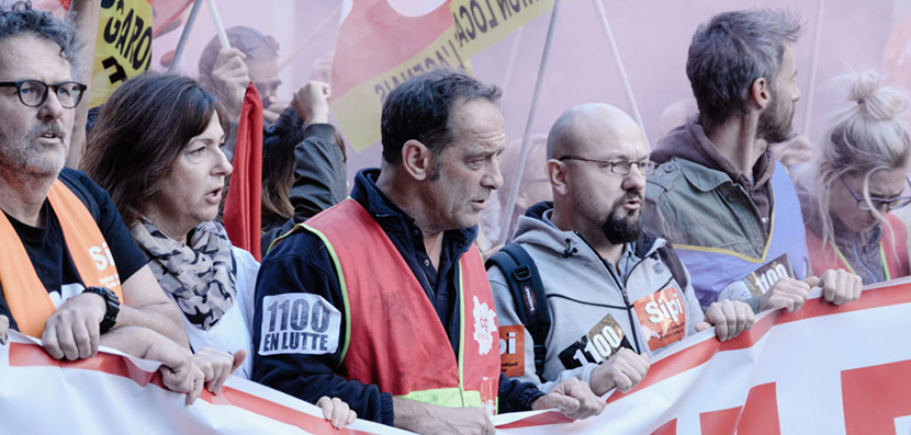 Characters from the film hold up a banner.