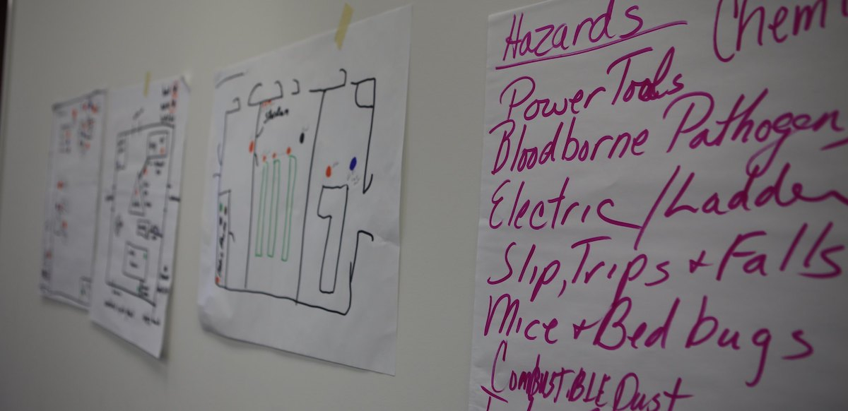 Flipcharts on the wall list workplace hazards including combustible dust and bloodborne pathogens