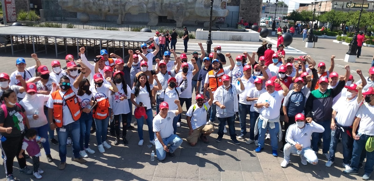 A group of fifty workers red hats and white shirts raise their fists and pose for the camera