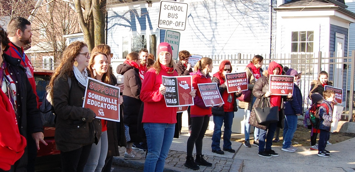 A crowd holding signs saying Support Somerville Educators and Living Wage for Paras