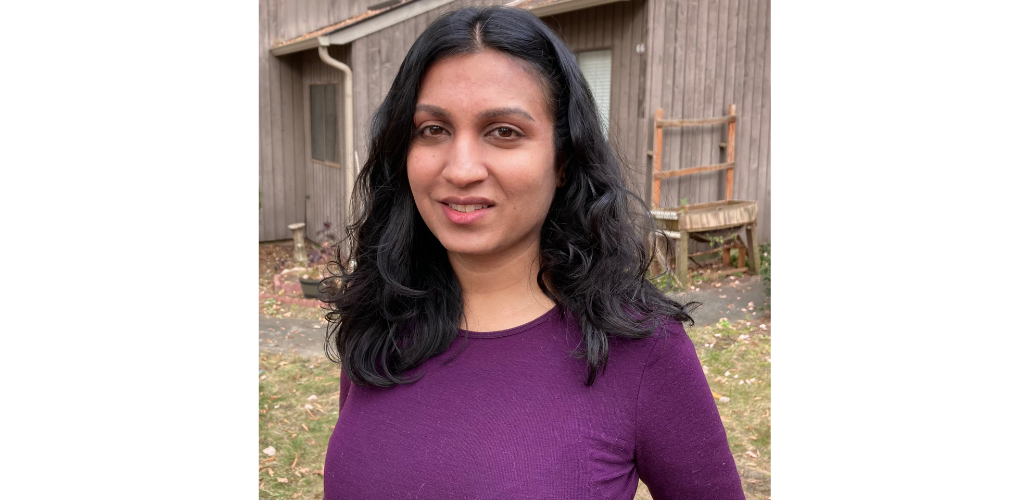 Sindhu poses outside in front of a barn. She has long black hair and is wearing a red shirt and a slight smile.