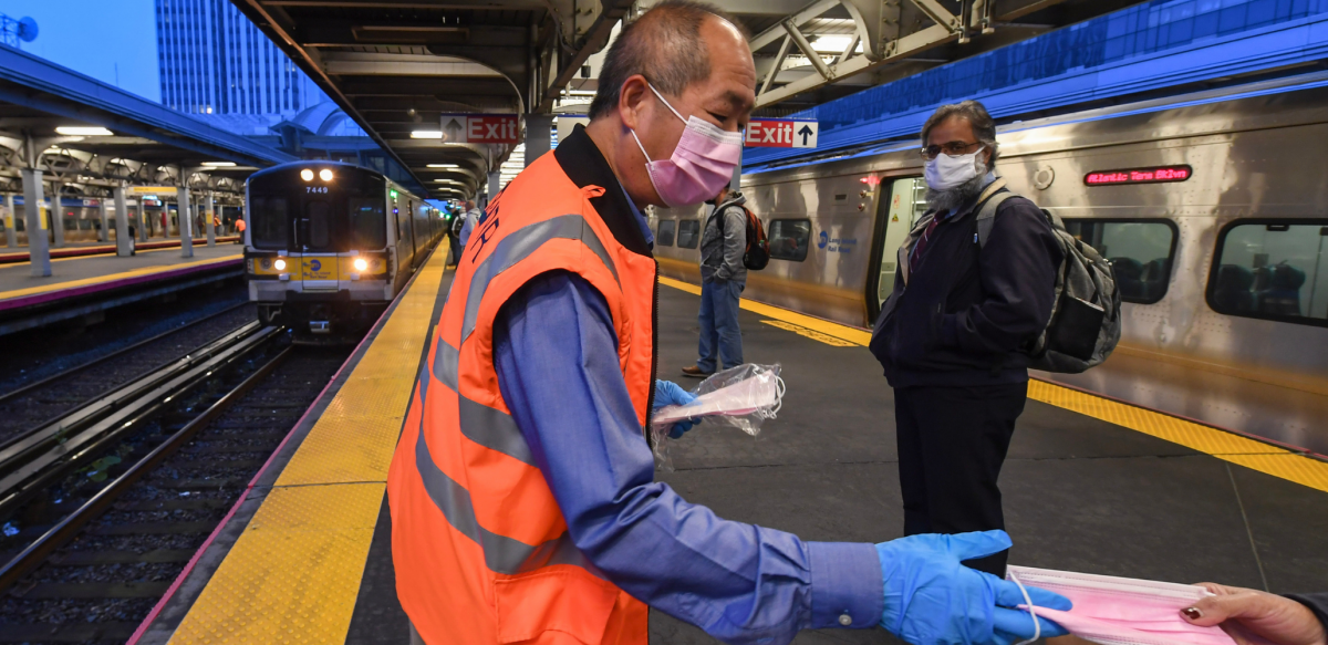 Man in orange vest hands out masks inside a train station