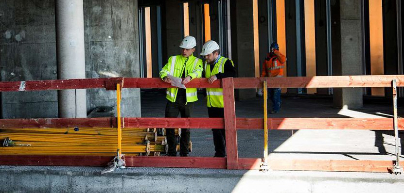 Two construction workers looking down in building construction site with wooden scaffolding around them.