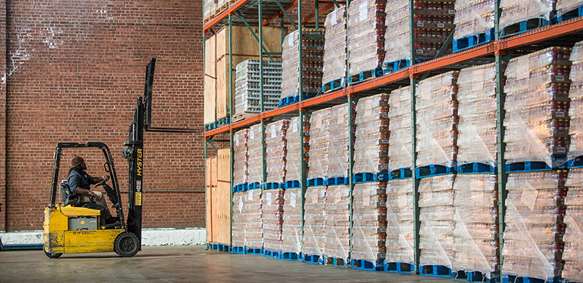 Worker with forklift in front of cases of pallets on shelves in warehouse