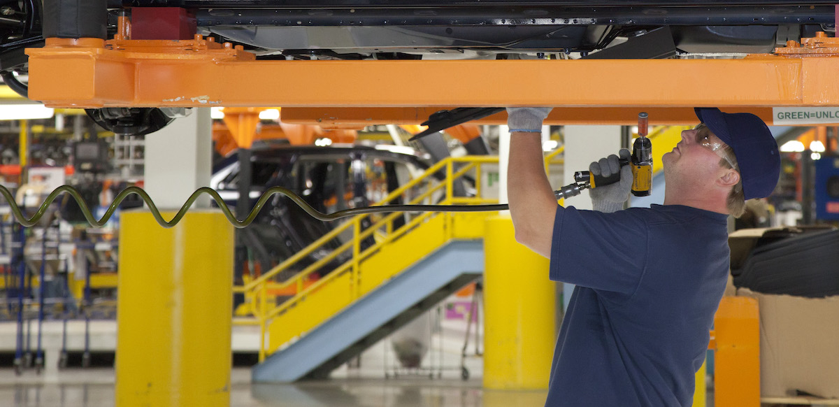 An autoworker tightens bolts on a car chassis above his head.