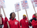 Five women and men in red hoodies that say “strike strike strike” hold picket signs