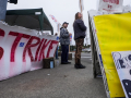 Two workers staff a picket line with a giant red ‘strike’ sign and a “Pension or Bust” sign.