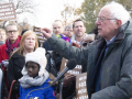 Bernie Sanders speaks at a podium surrounded by people holding signs about housing