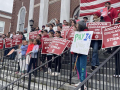 A large group of teachers stand in the steps of a large brick building holding red signs that say “Andover Educators on Strike” 