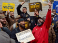 A group of excited Teamsters, some in brown uniforms, others in union hoodies,  hold signs saying time to pay up,